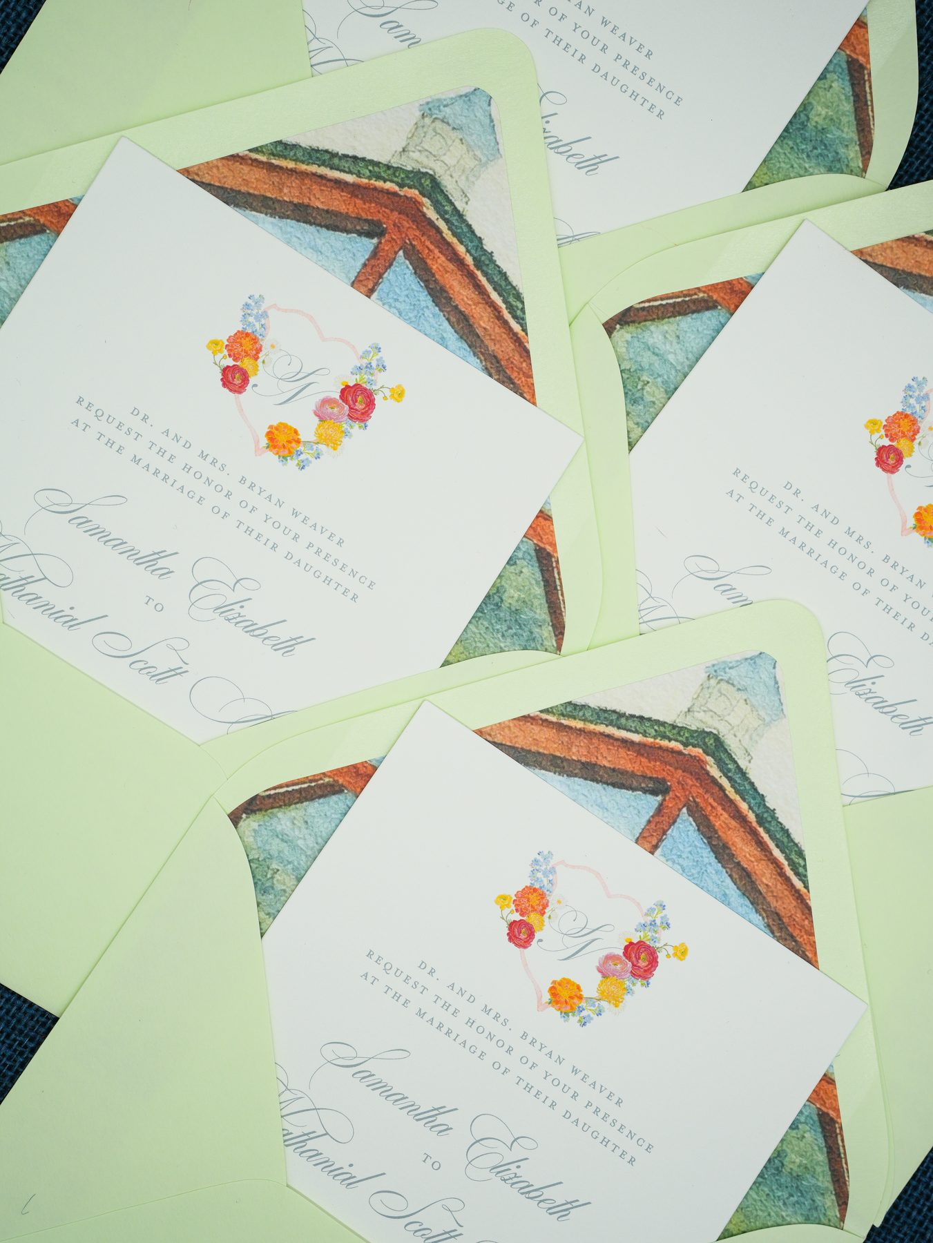 Layered coral floral monogram invitations resting on mint envelopes lined with a watercolor chapel illustration.