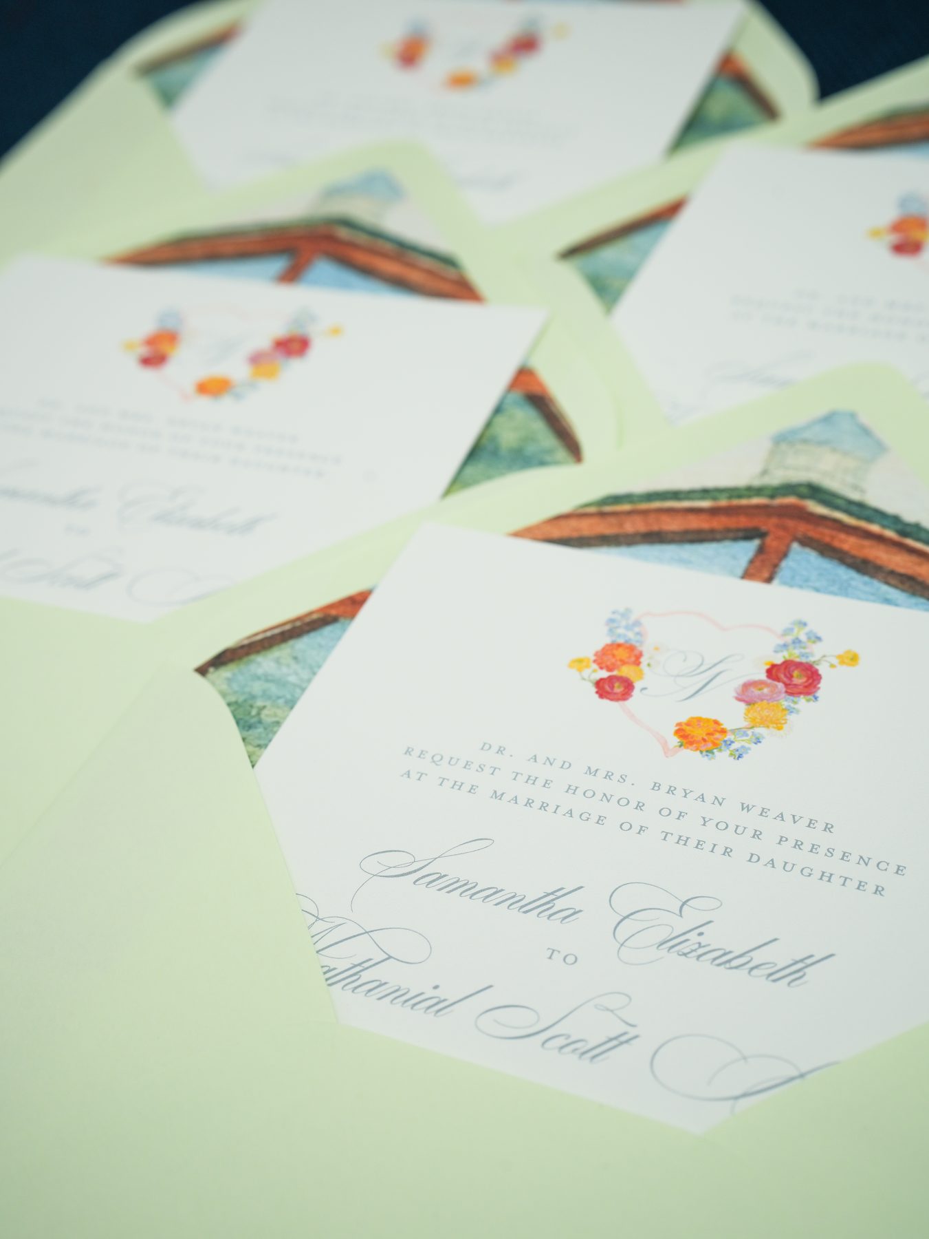 Coral and blue floral wedding invitations fanned over soft mint envelopes lined with a watercolor chapel illustration.