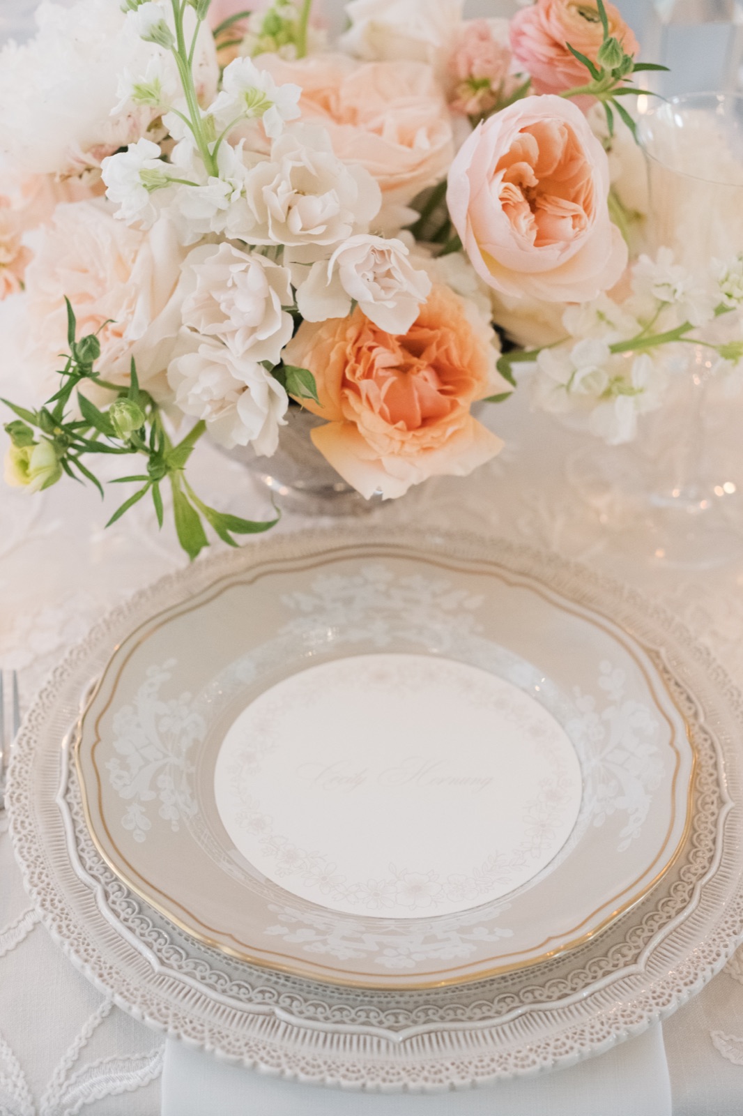 A delicate place setting with custom calligraphy on the salad plate, surrounded by blush florals and a lace tablecloth.