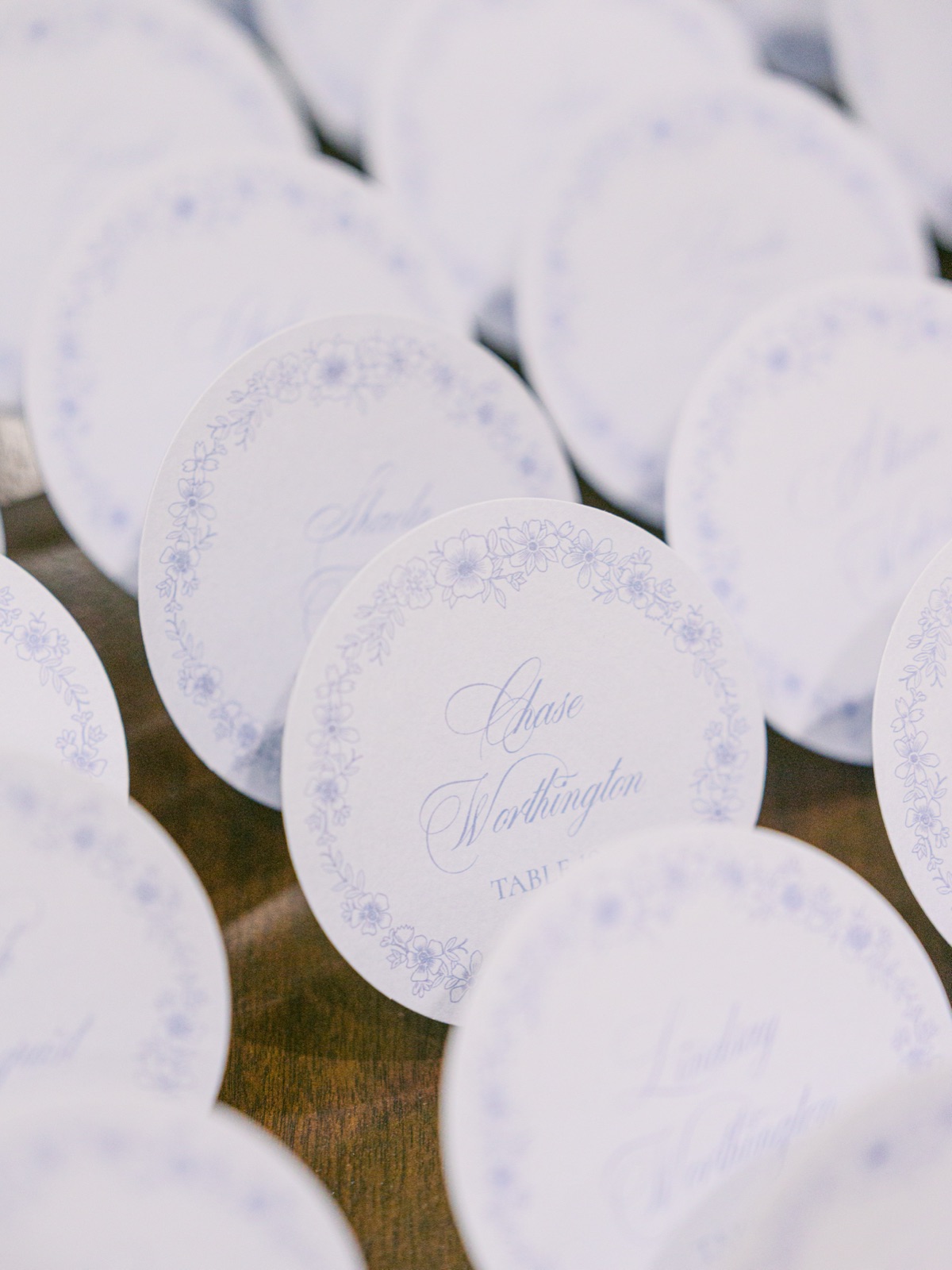 Close-up of round wedding escort cards with delicate blue floral borders and calligraphy.