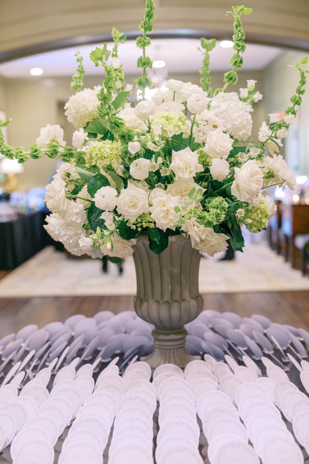 A grand white and green floral arrangement in a stone urn anchoring a table of round escort cards.
