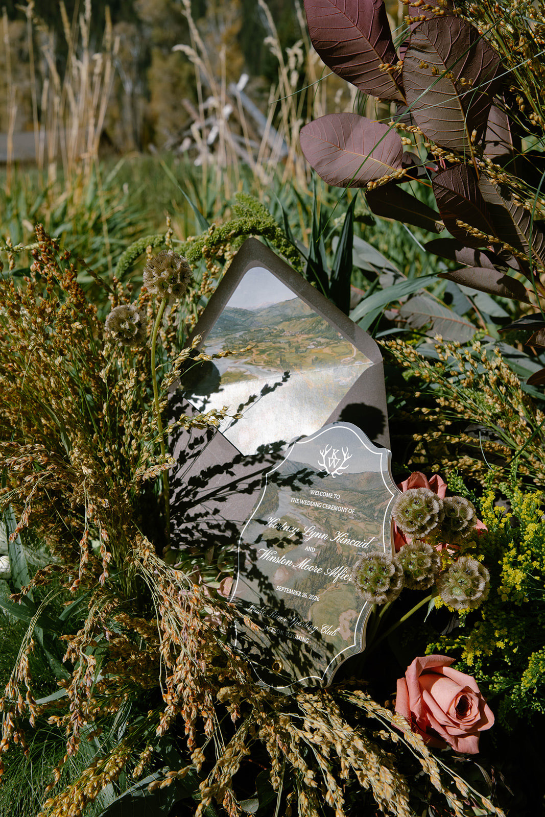 A die-cut acrylic place card printed with a mountain landscape, nestled in florals.