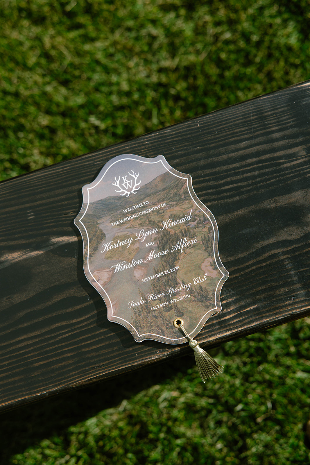 A die-cut acrylic welcome card with an antler crest resting on a dark wood bench.