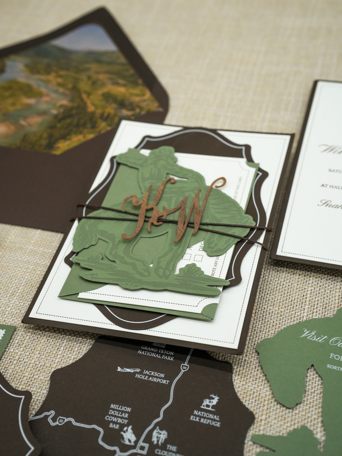 The invitation bundle tied with twine and a wood monogram over the die-cut cowboy band.