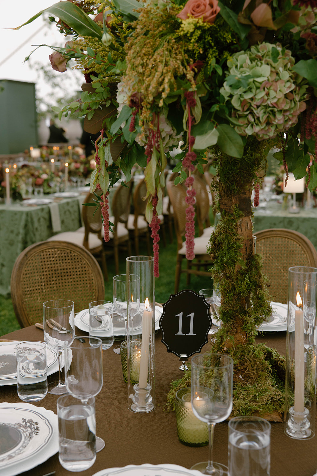 A towering greenery and hydrangea centerpiece above a table marked eleven.