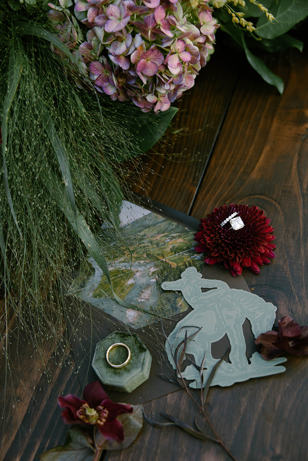 A die-cut cowboy place card on dark wood with a single dried bloom.