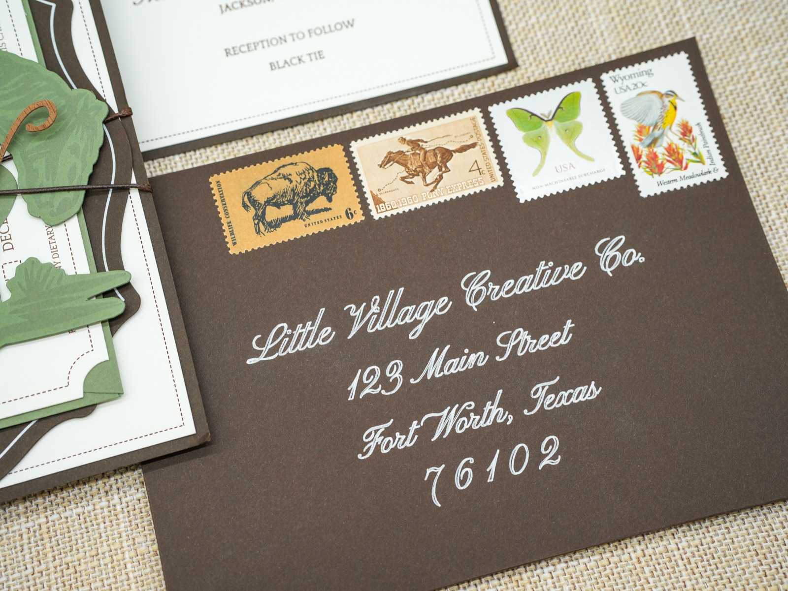 A chocolate brown envelope addressed in white calligraphy, dressed with vintage western stamps.