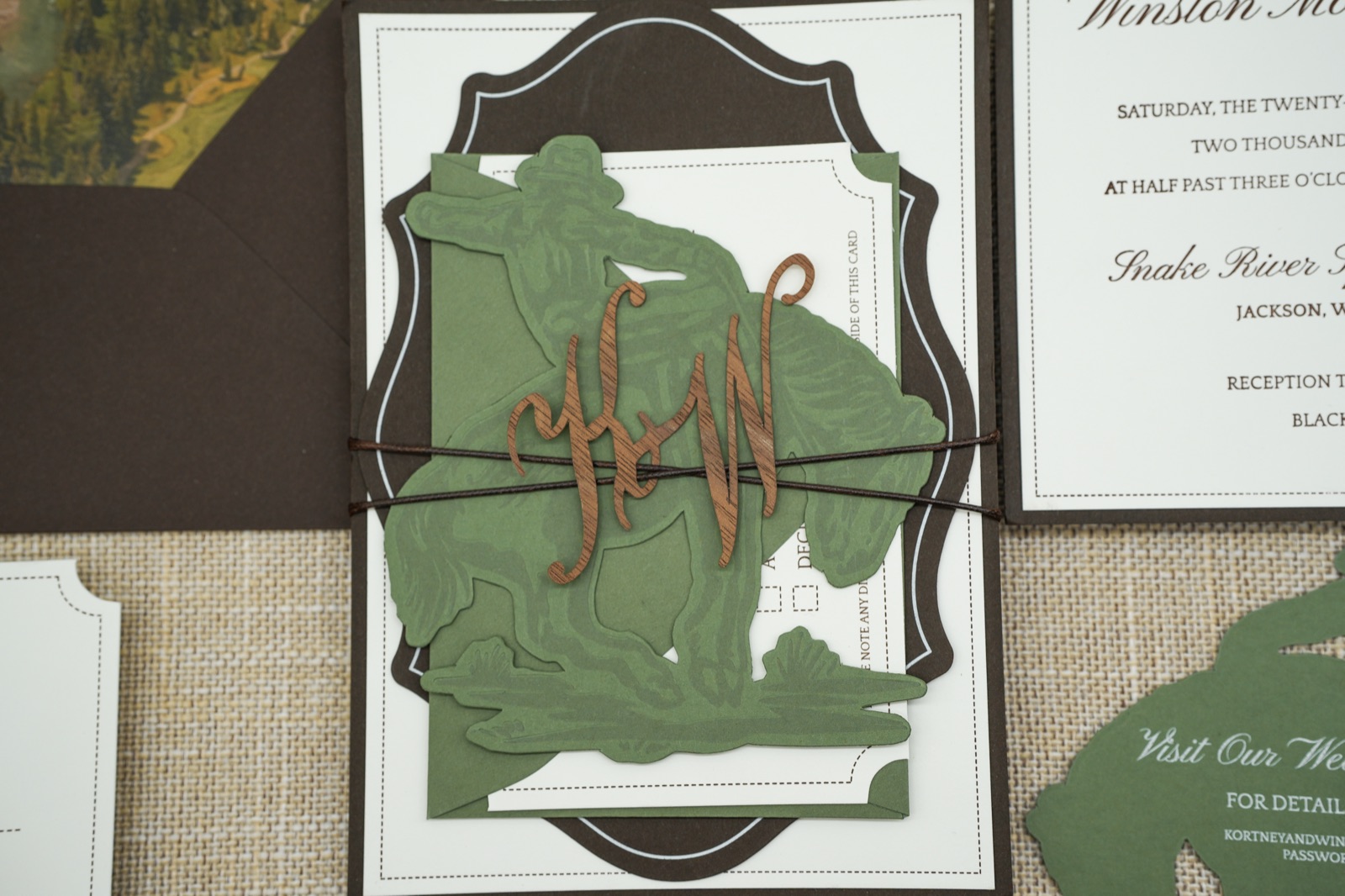 The invitation stack wrapped with the sage bronc rider band and copper monogram.