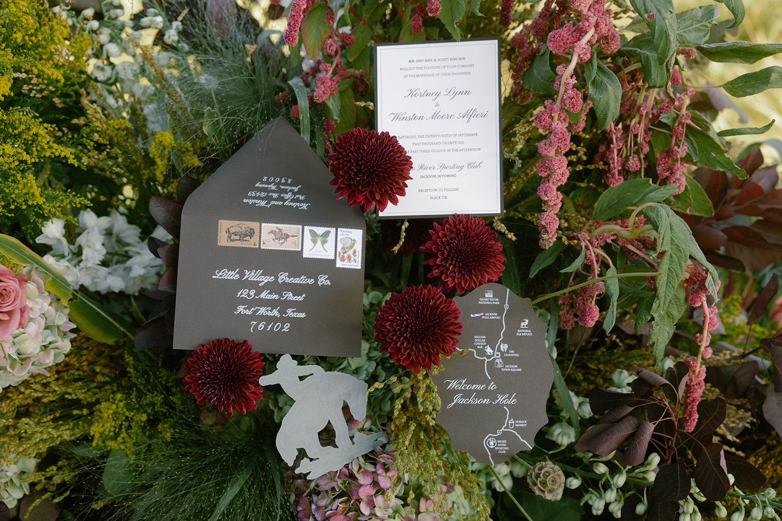 The letterpress invitation nestled in an arrangement of burgundy dahlias and trailing blooms.