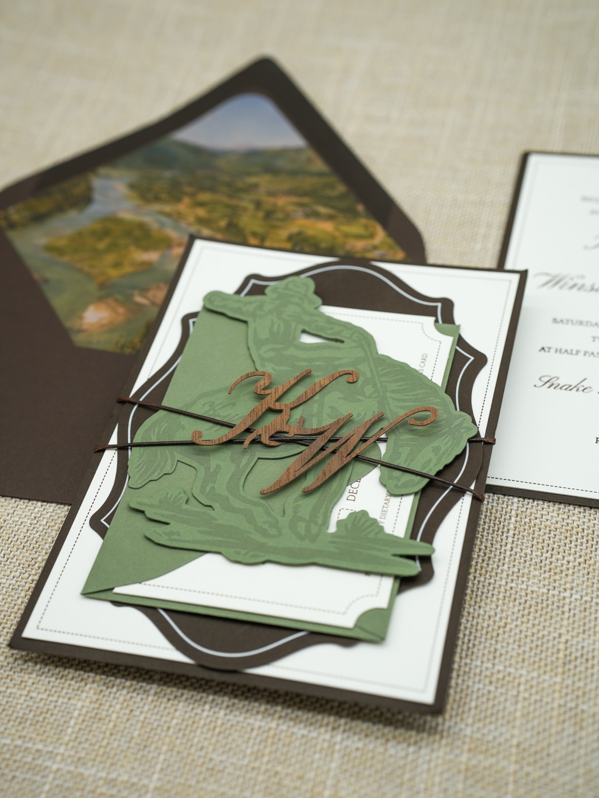 The copper monogram and bronc rider band tied over the invitation stack.