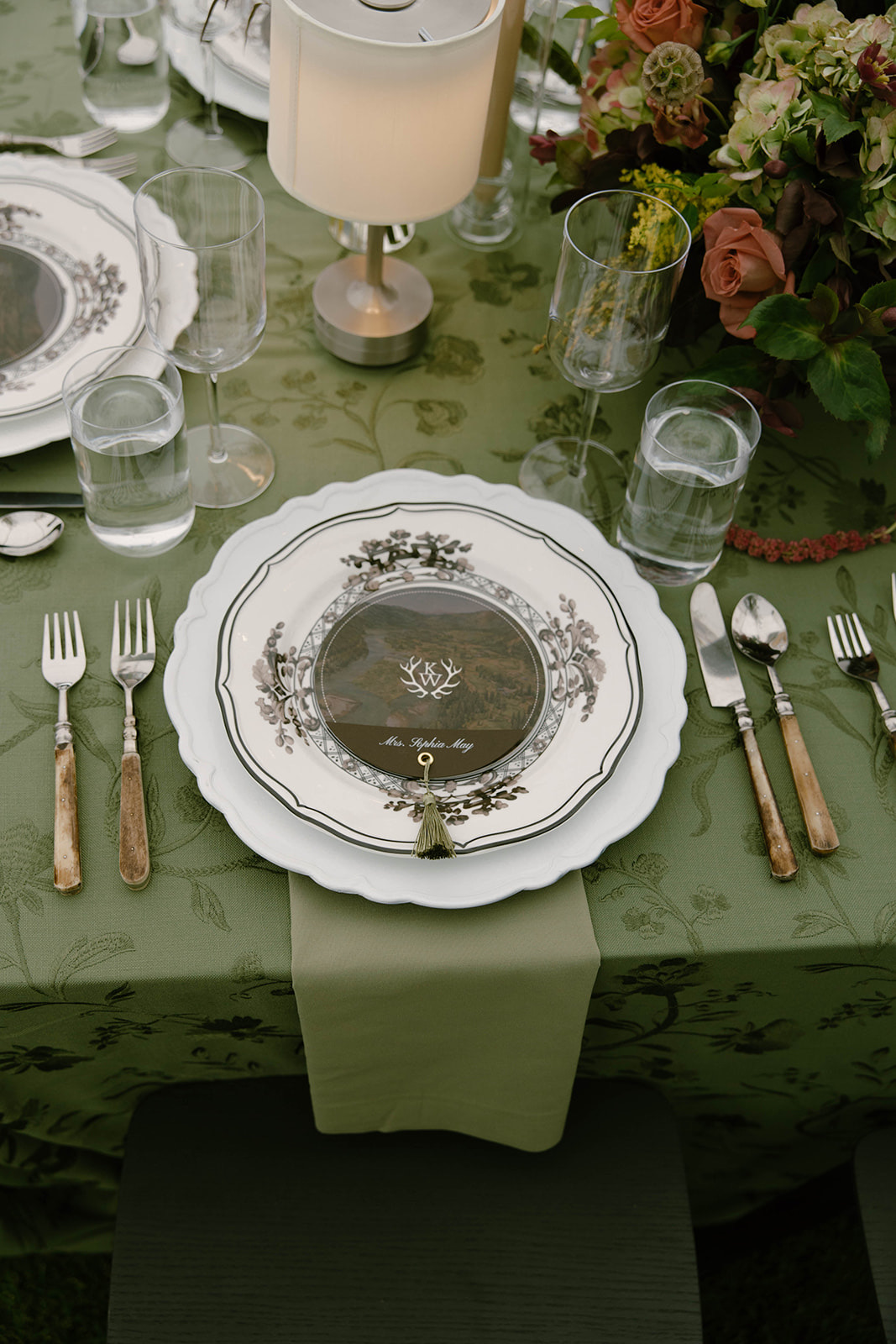A place setting of botanical-bordered china on sage damask with gold flatware.