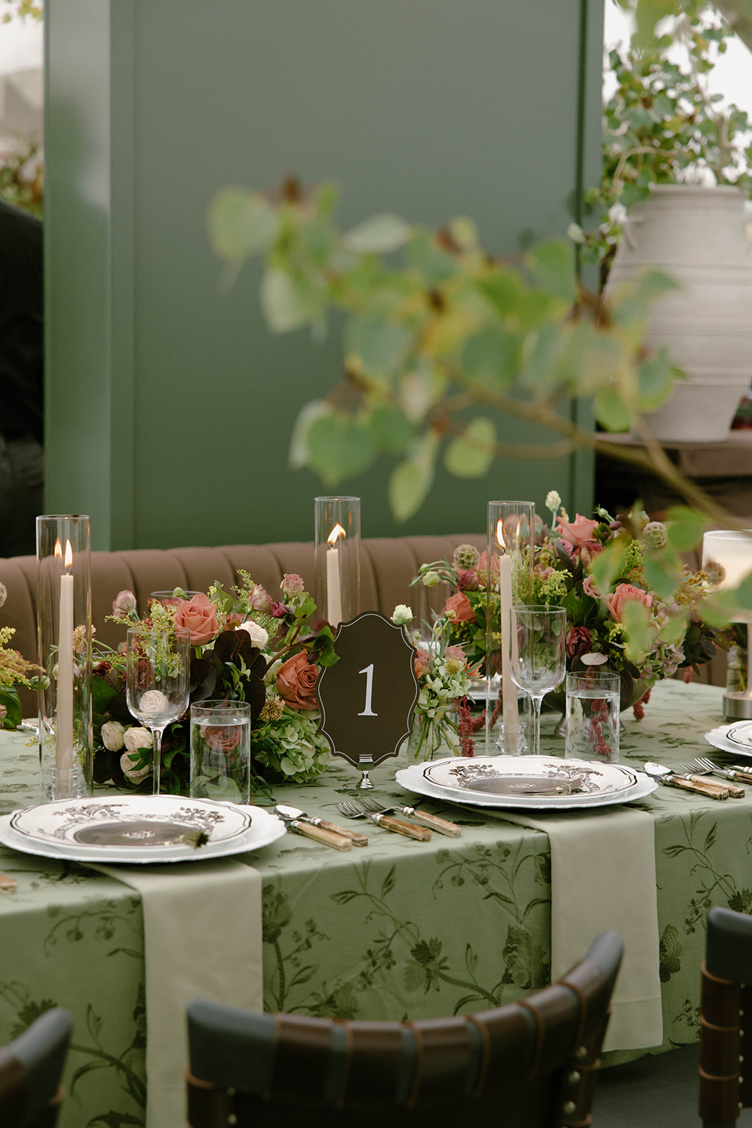 A reception table in sage floral linen with botanical china and a letterpress table number.