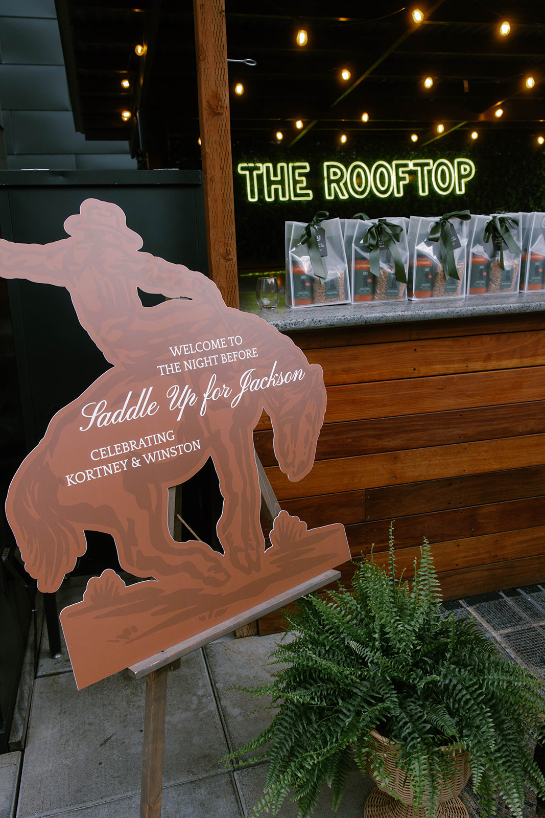 A wood bronc-rider welcome sign lettered 'Saddle Up for Jackson' beside a fern at the reception entrance.