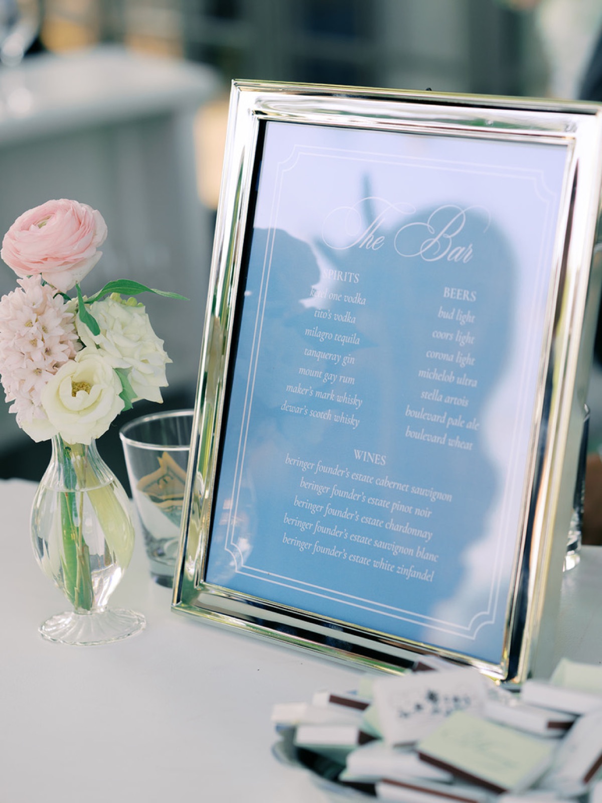 A framed bar menu in soft blue beside a bud vase of ranunculus.