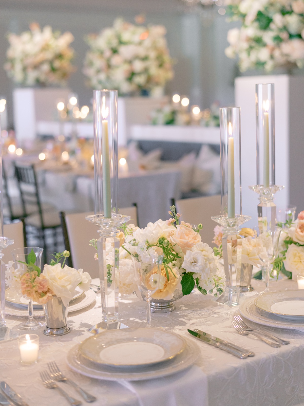 Reception tables glowing with taper candles, peach florals, and round menus at each place.