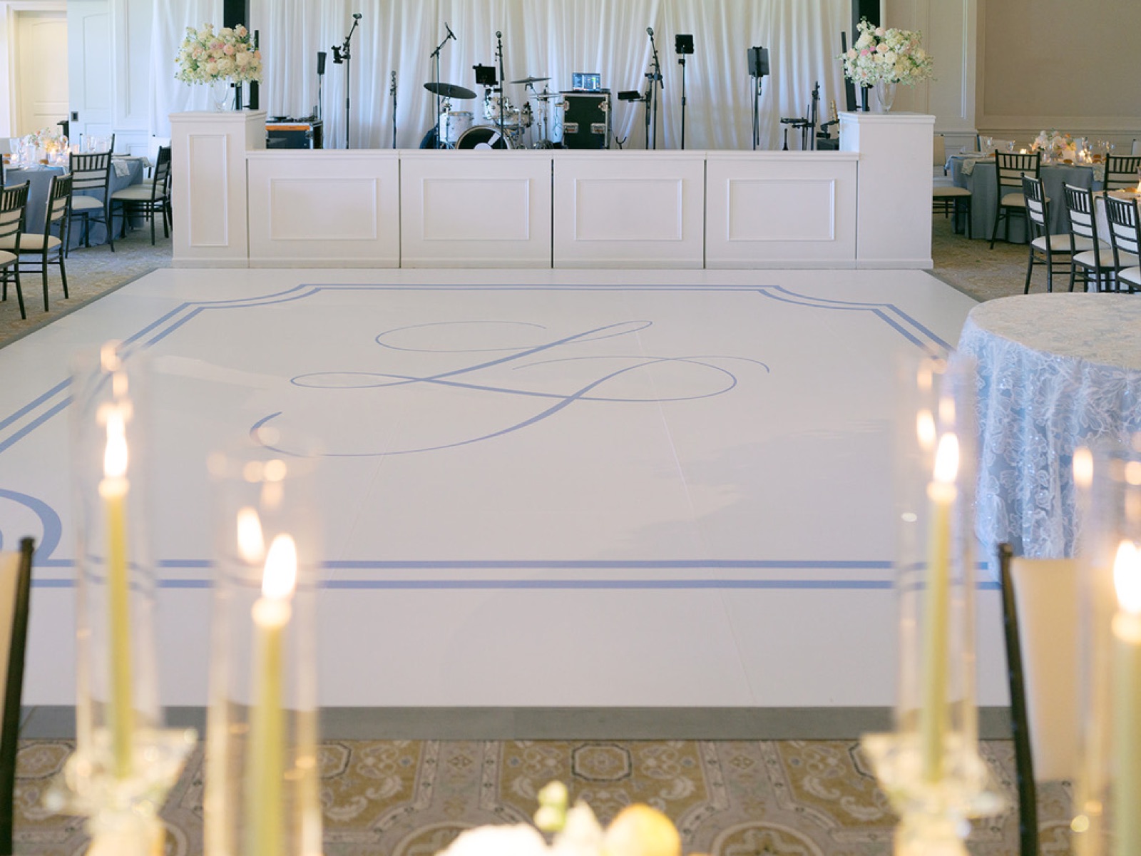 A white dance floor painted with the couple's monogram inside a soft blue double border.