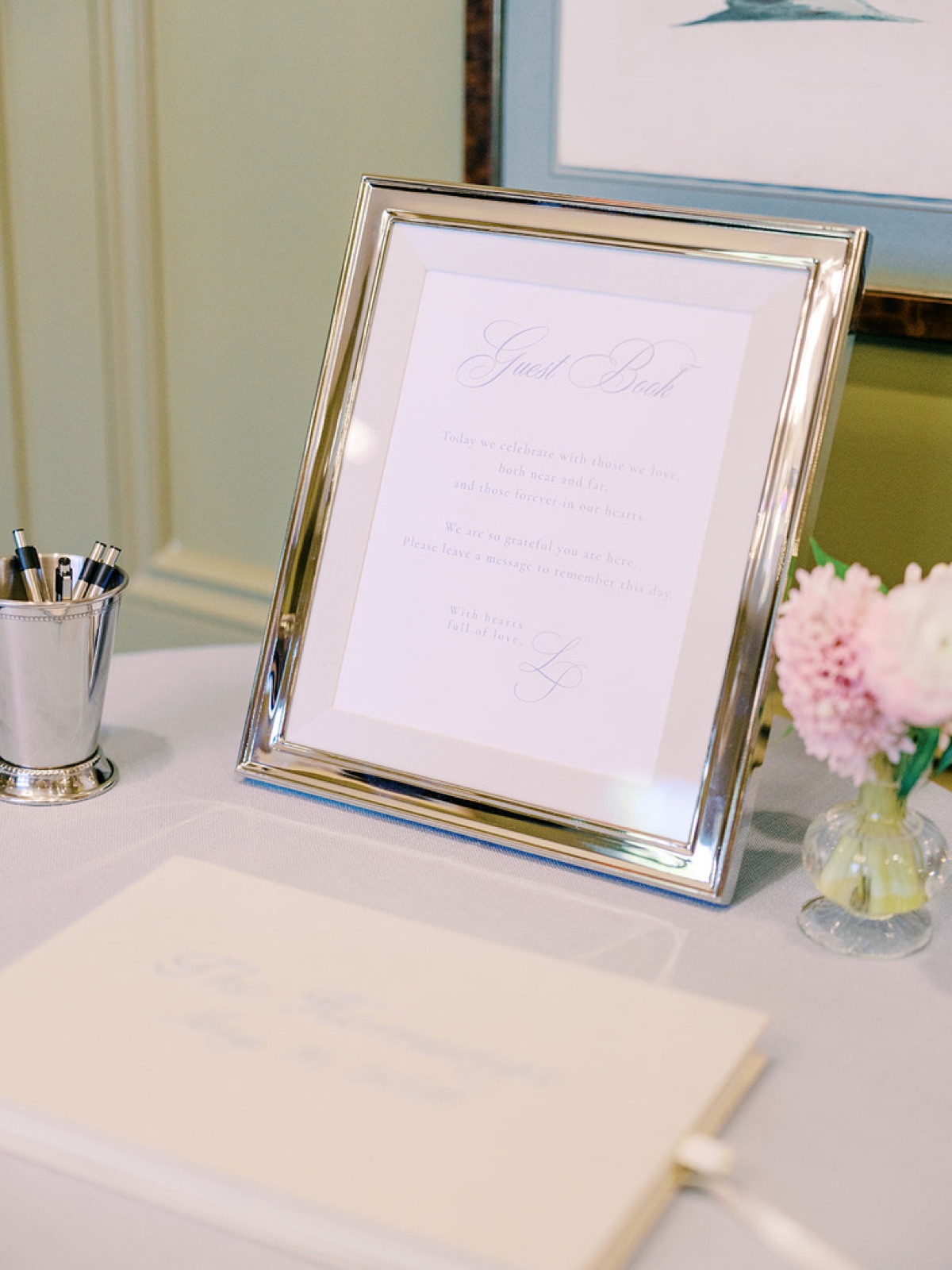 The guest book table with a framed welcome note, a silver cup of pens, and pink hyacinth.