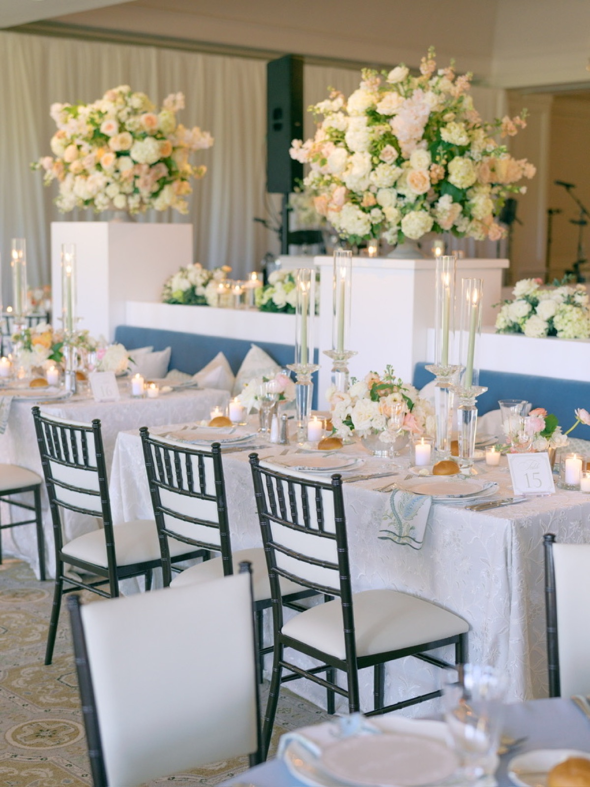 Reception tables in lace and blue beneath towering white and peach arrangements.
