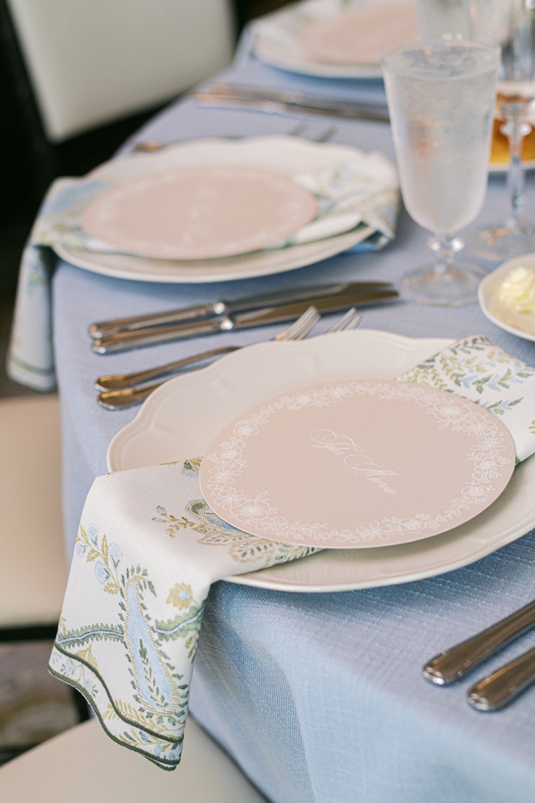 A place setting with a paisley-embroidered napkin and round menu on pale blue.