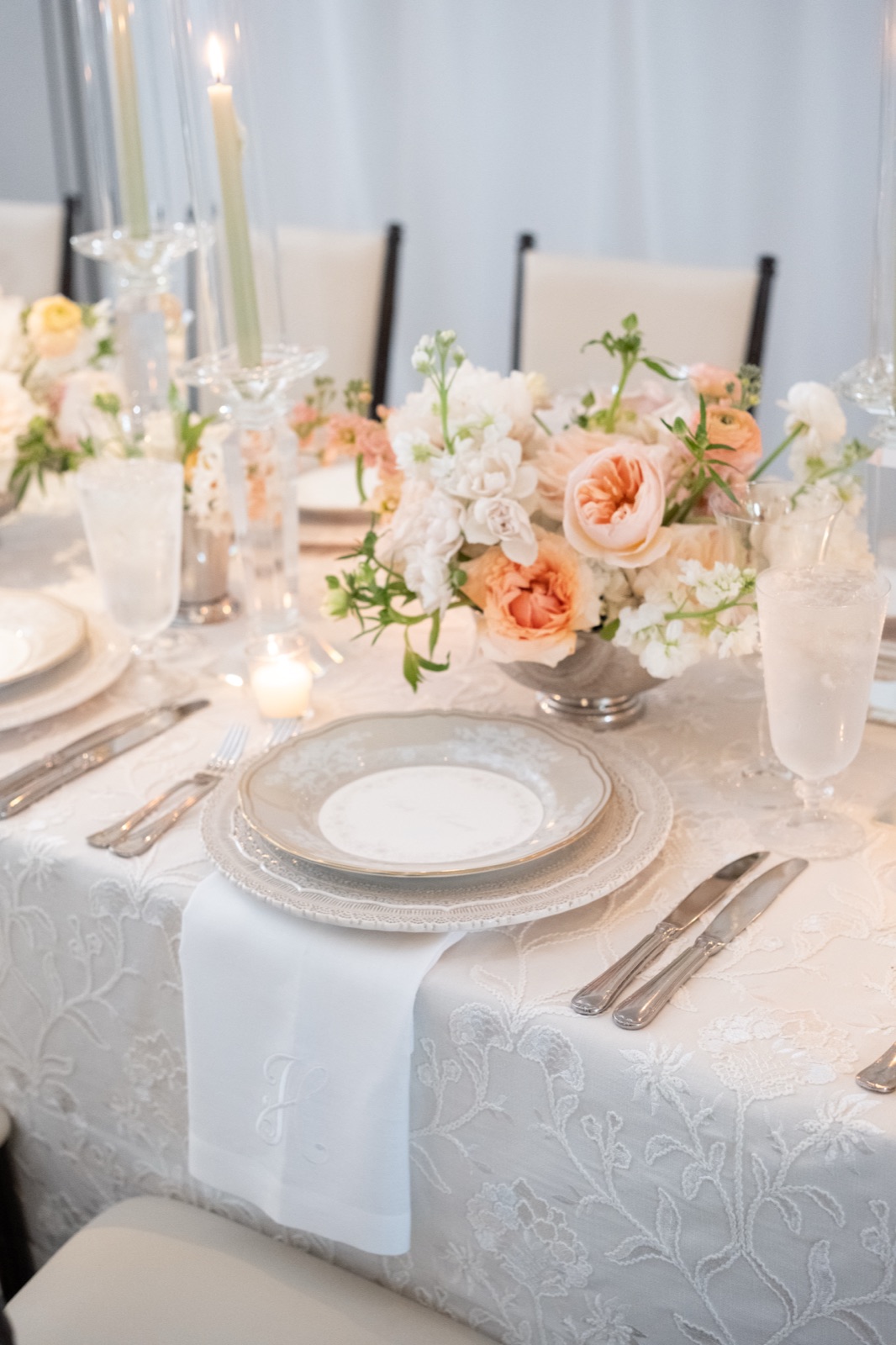 A place setting with layered lace china beside garden roses in peach and cream.