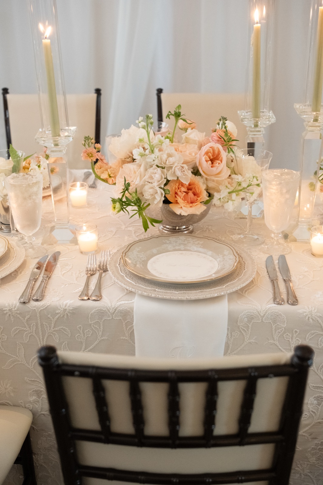 A reception chair and place setting framed by candlelight and soft peach centerpieces.