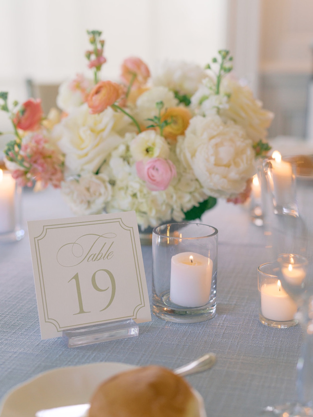 A framed table number amid blush ranunculus and candlelight.
