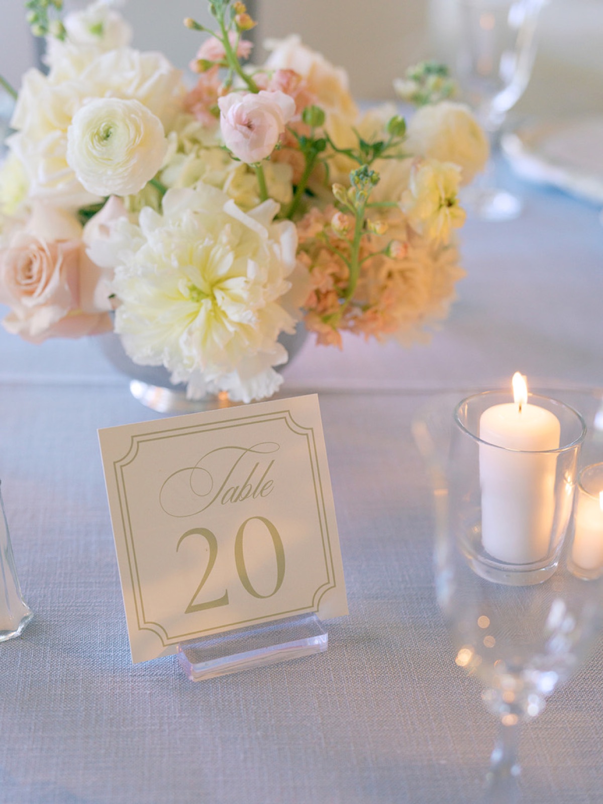 A gold-bordered table number beside soft peach florals on blue linen.