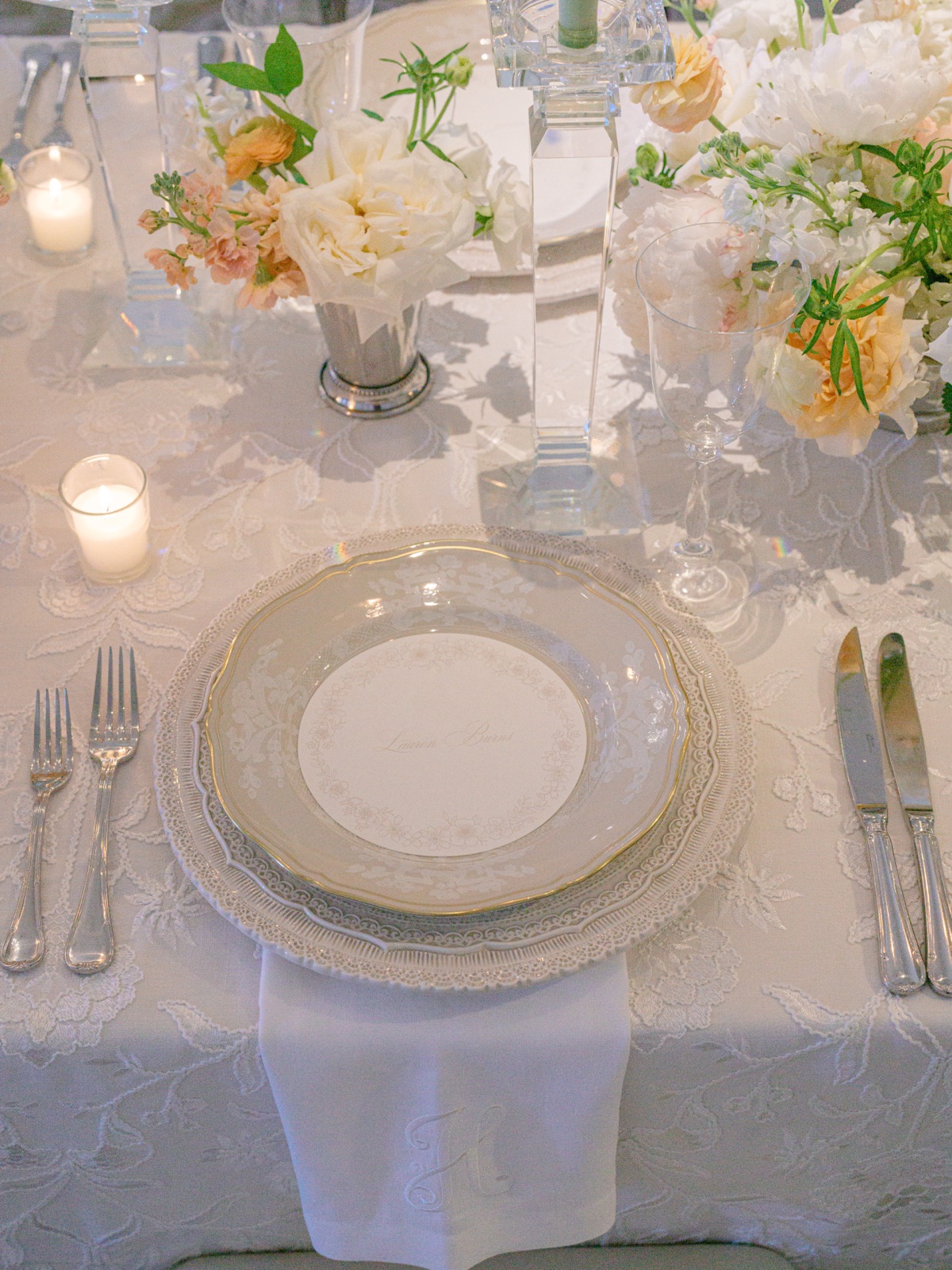 A custom calligraphy place card set on gold-rimmed china over an embroidered linen tablecloth, by Little Village Creative Co.