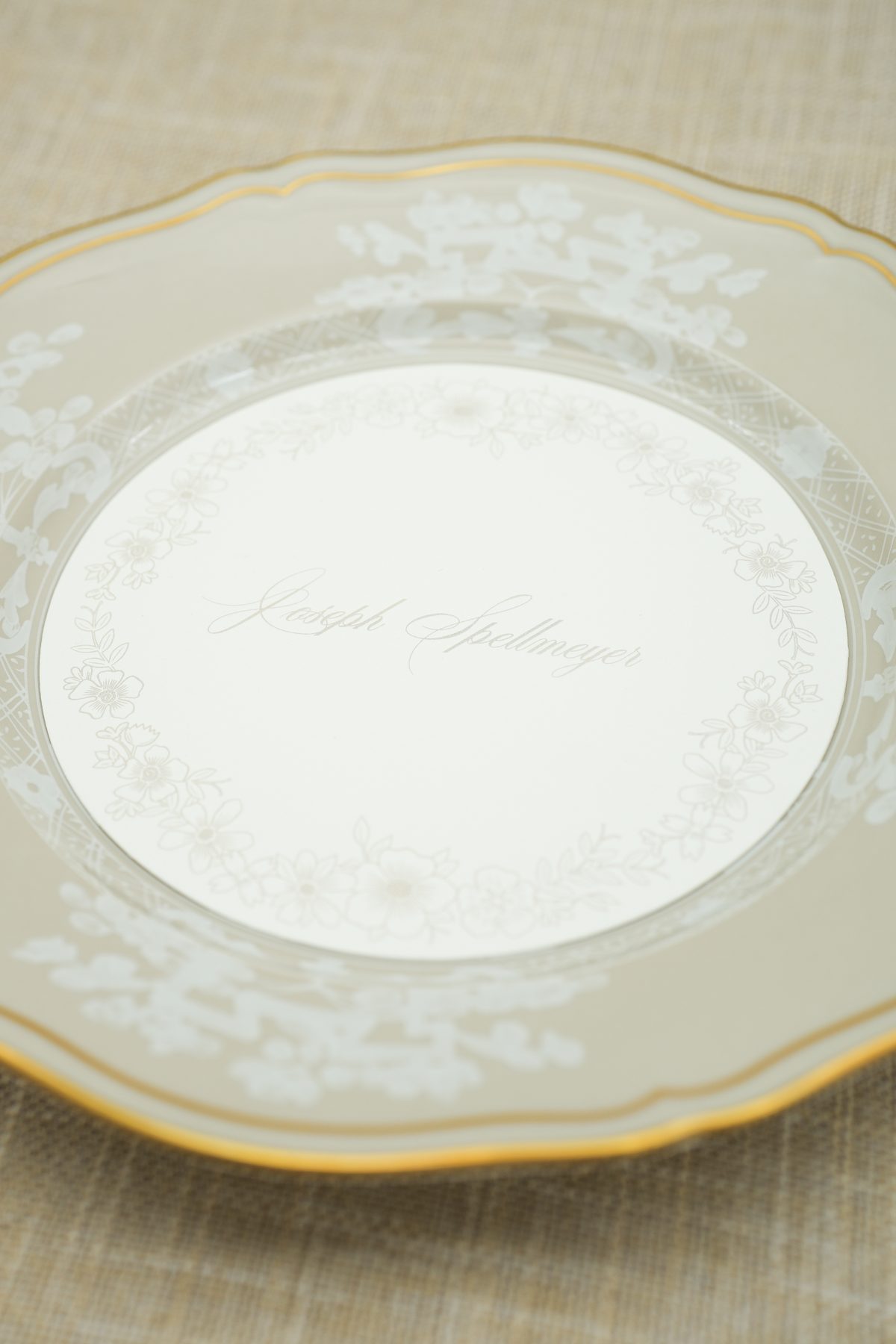 A round wedding menu printed in soft floral motifs resting inside a gold-rimmed china plate.