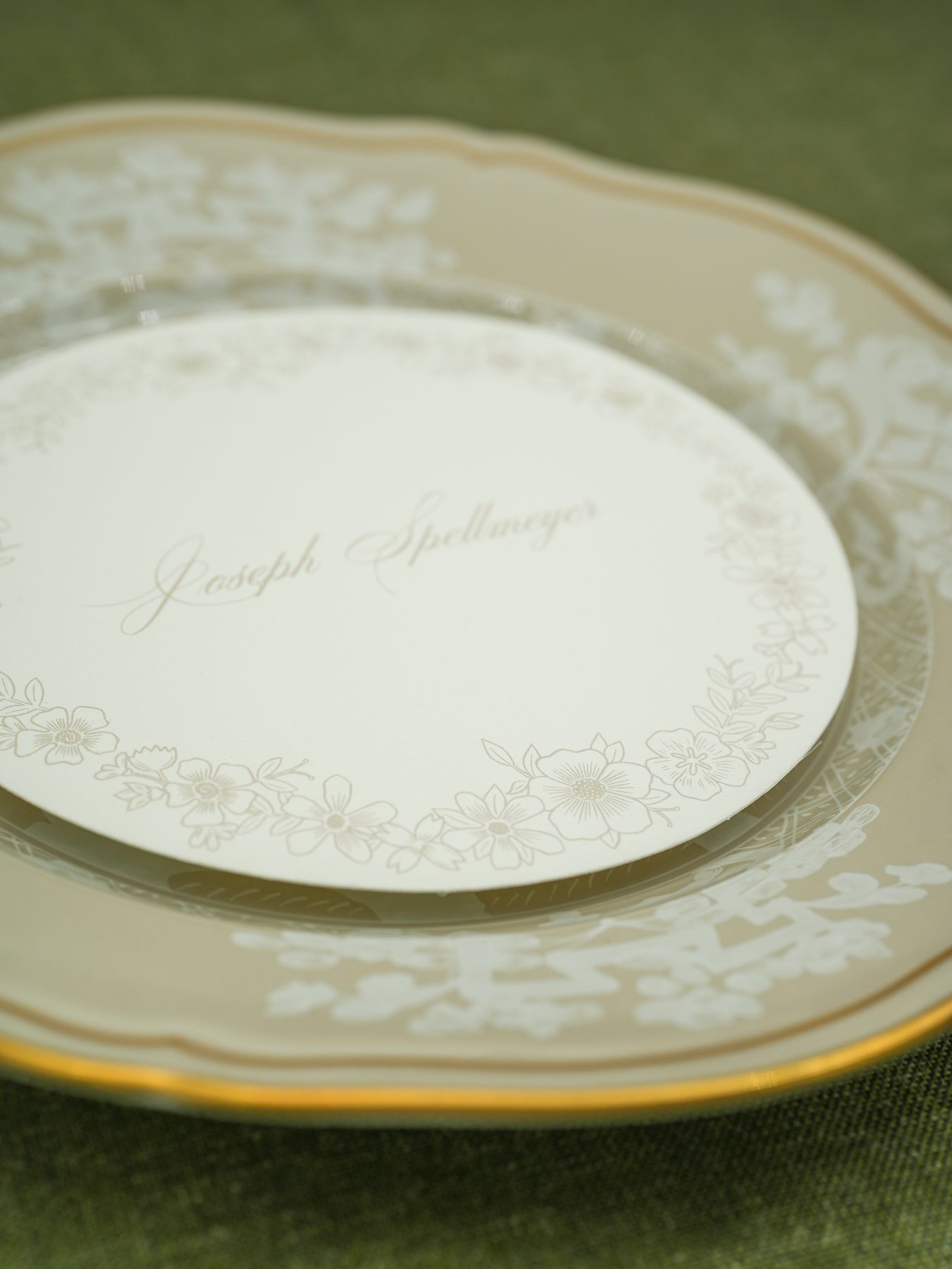 A round wedding menu in cream with a delicate floral border and a guest's name in script calligraphy across the center.