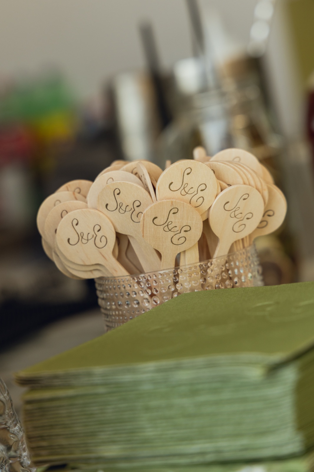 Monogrammed drink stirrers beside a stack of sage napkins.