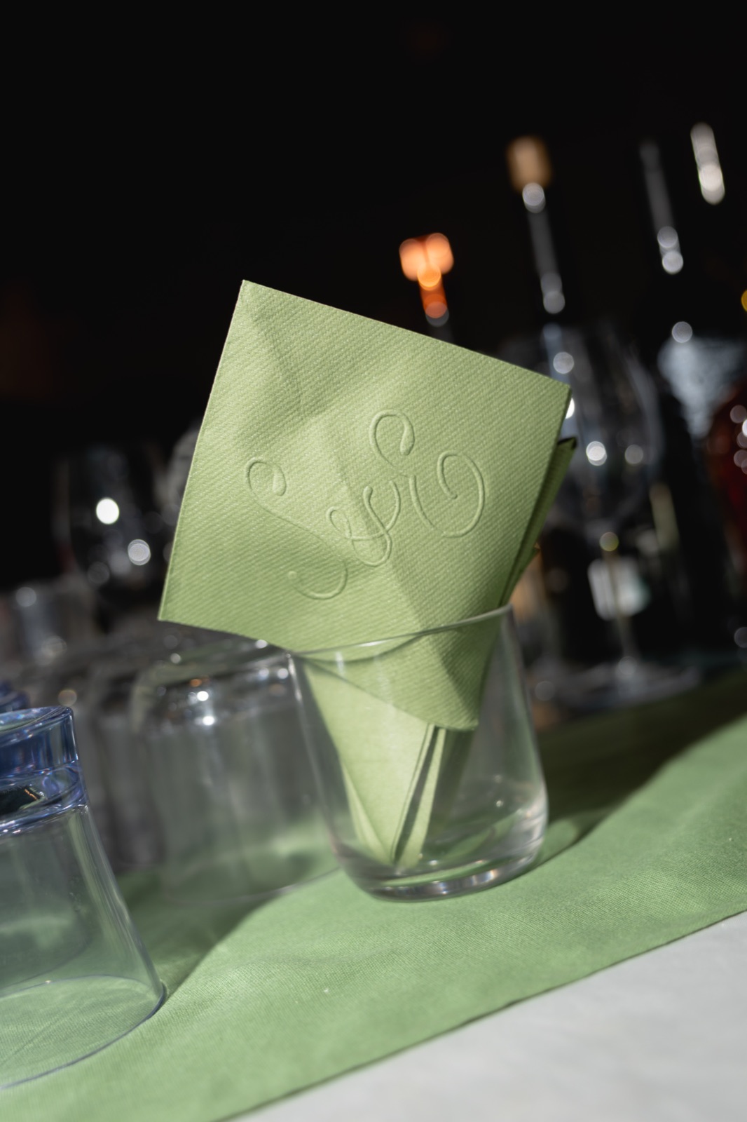 An embossed sage napkin tucked into a glass at the bar.