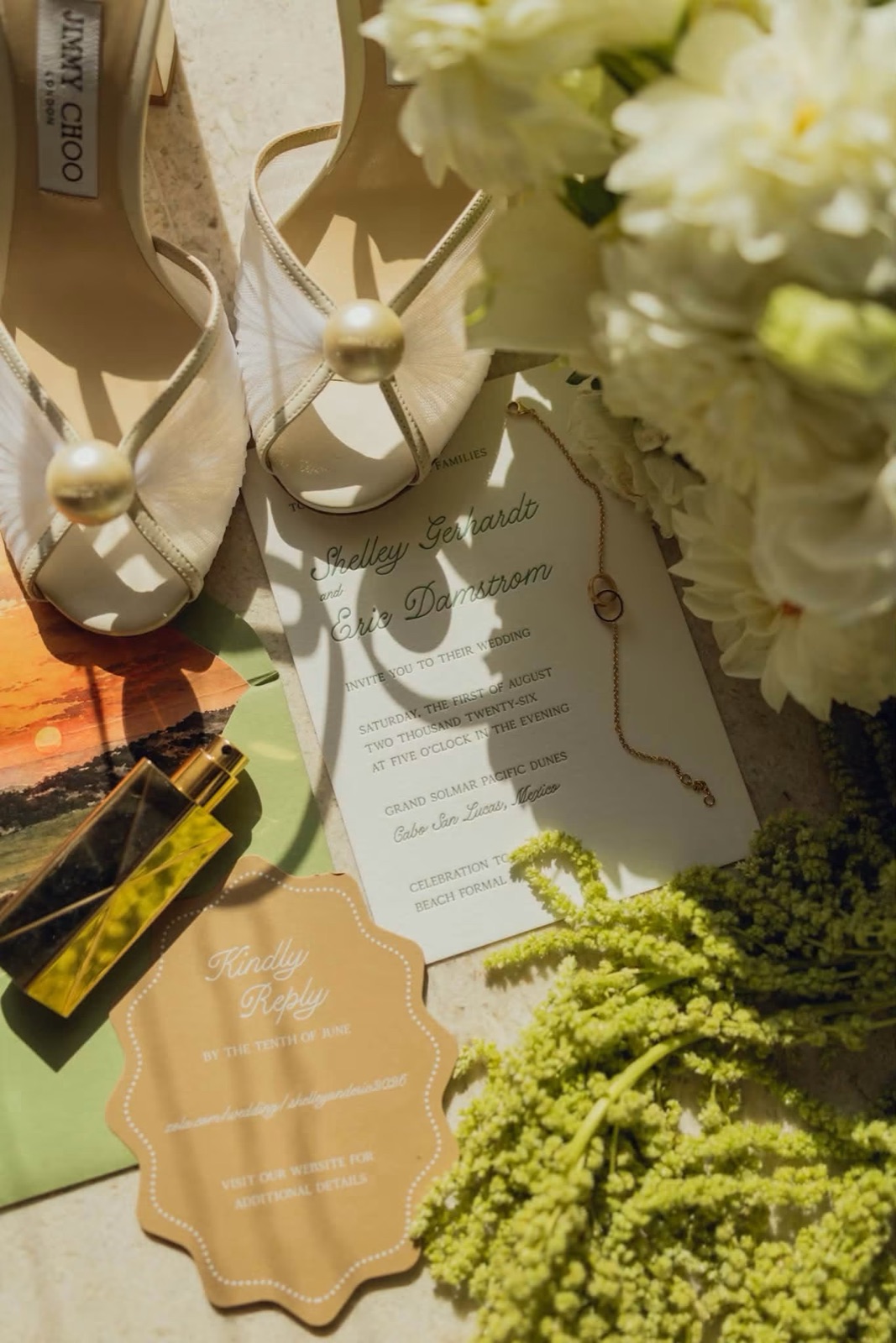 The invitation with its kraft tag styled among white florals and pearl heels.