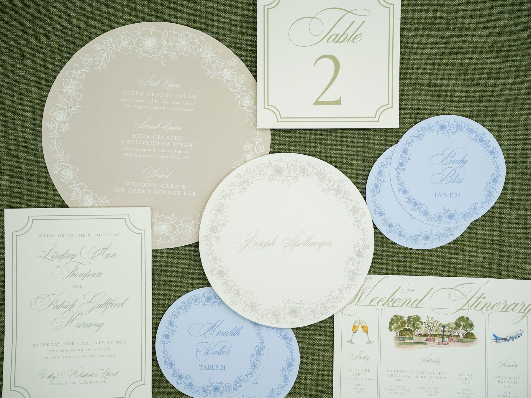 A garden wedding day-of suite with letterpress invitation, round taupe menu, soft blue round place cards, gold-framed table number, and a weekend itinerary featuring a watercolor venue scene.