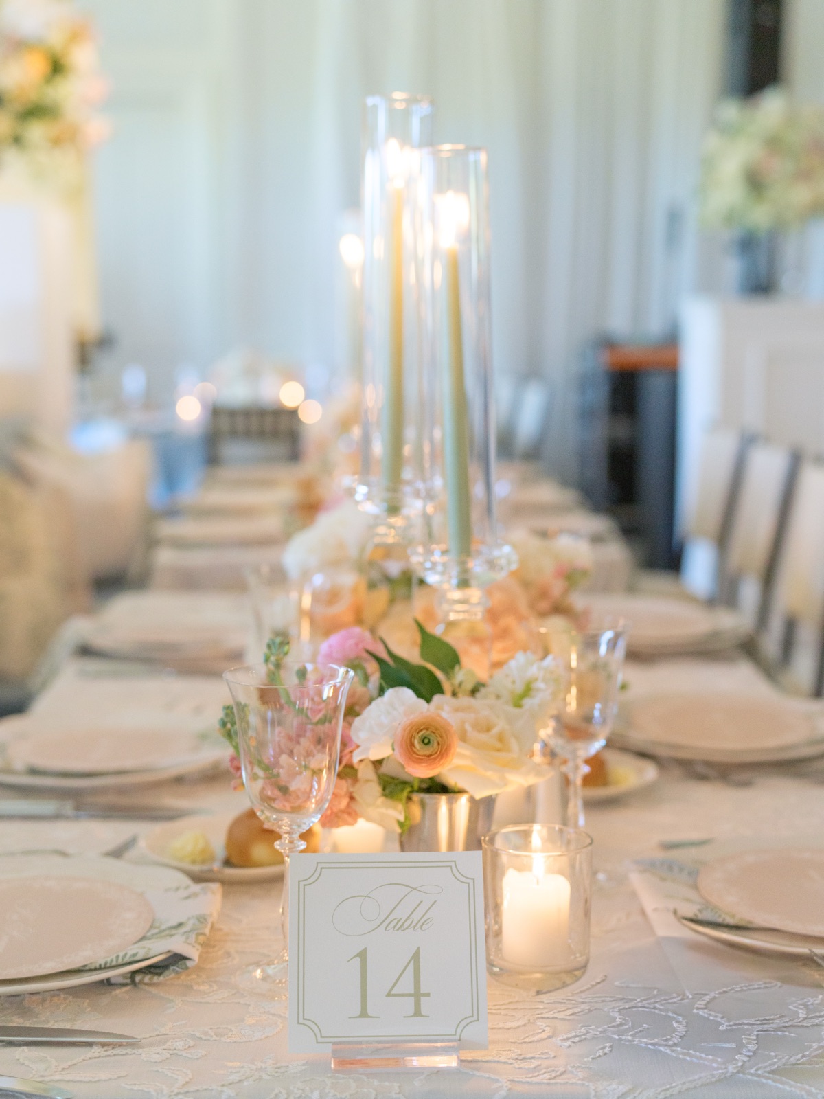 A framed wedding table number on a long reception table with crystal candleholders and pastel floral centerpiece.
