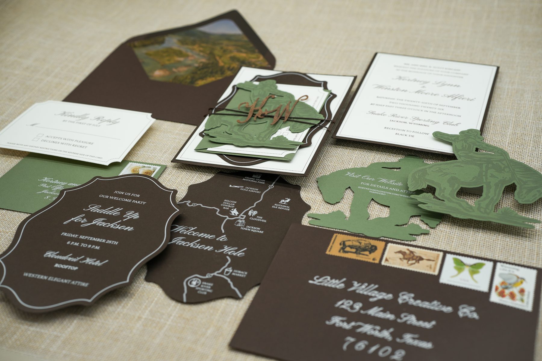 A close-up of the hunter-green western suite, layering the watercolor map envelope liner, die-cut sage cowboy silhouettes, and dark brown stationery.