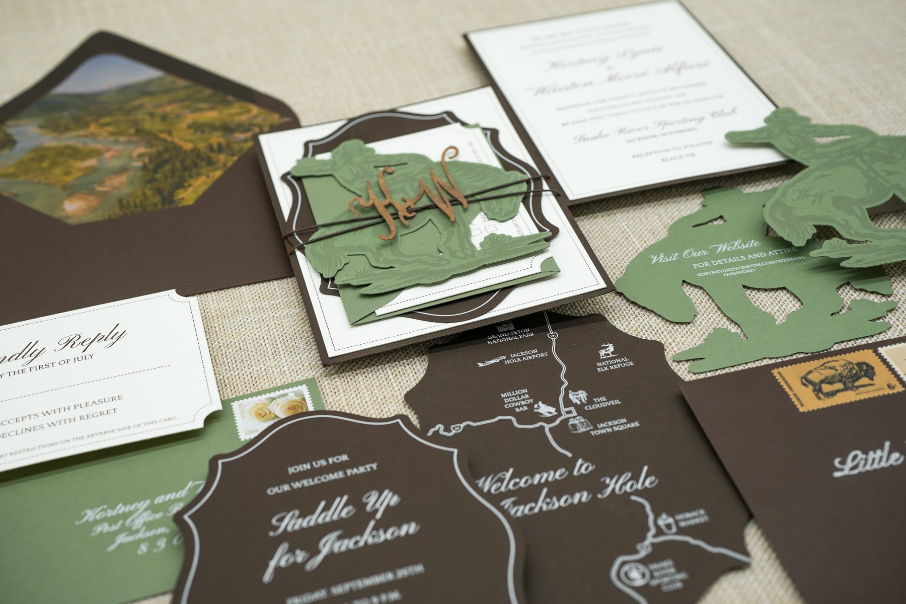 Tighter view of the hunter-green custom wedding suite, layering the watercolor liner, sage cowboy belly band, and reply card.